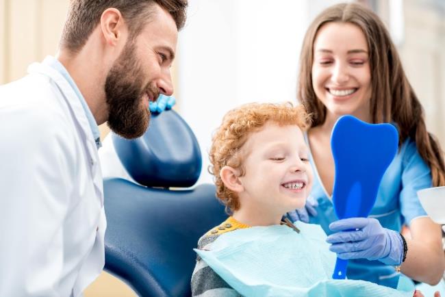 ילד מחייך למראה אחרי טיפול שורש מוצלח ולידו רופא השיניים והסייעת