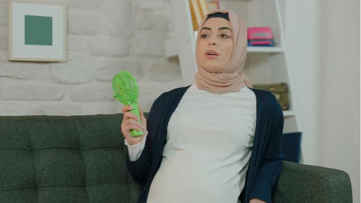אישה ערבייה בשבוע 40 להריון שסובלת מחום יושבת עם מאוורר קטן