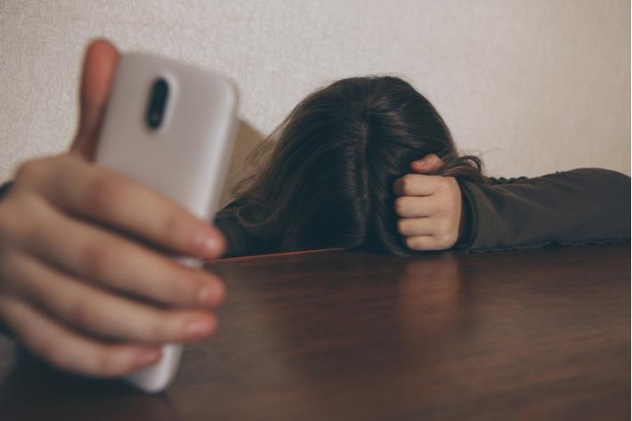 ילדה סובלת מדיכאון מול הטלפון אחרי תקופה של סגרים בגלל הקורונה