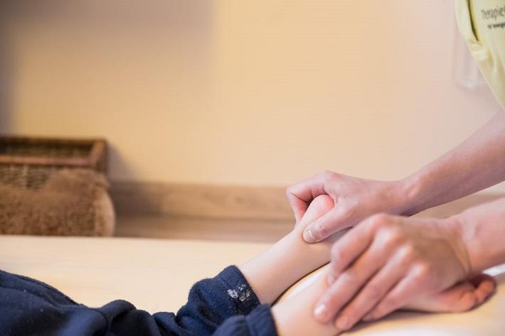 ידיים של רפלקסולוגית מבצעות טיפול לילד שוכב במסגרת טיפולים משלימים לילדים
