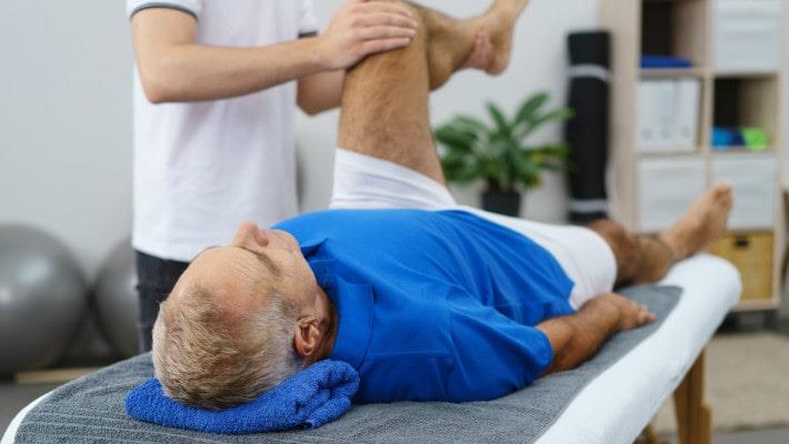פיזיותרפיסט תוצך ברגלו של מטופל שוכב בזמן פיזיותרפיה