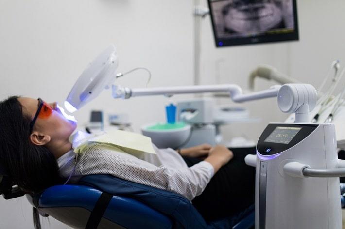 מטופלת שוכבת על כיסא רופאת שיניים בזמן הלבנת שיניים בלייזר