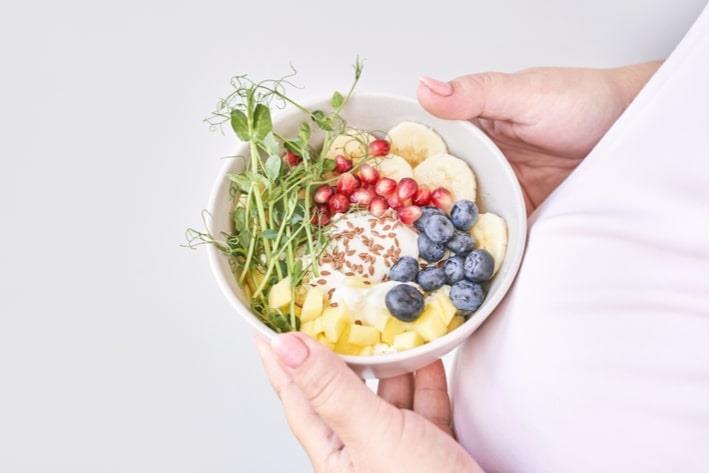 אישה בשבוע 22 להריון מחזיקה קערית עם מזון עשיר בסידן ואשלגן