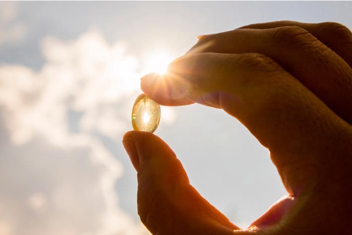 אישה מחזיקה בידיה תוסף ויטמין D ופונה לשמש - מקור טבעי לויטמין 