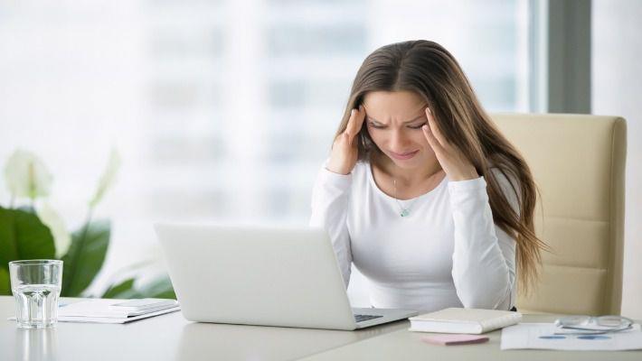 אישה סובלת מכאב ראש יושבת ליד שולחן העבודה שלה