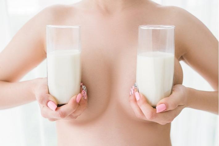 אישה בשבוע 32 להריון מחזיקה שתי כוסות חלב ליד החזה שלה