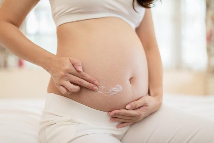 אישה בשבוע 23 להריון מורחת קרם לחות על הבטן