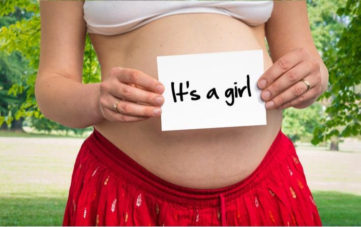אישה בשבוע 16 להריון מחזיקה על הבטן פתק שכתוב בו באנגלית שזו בת