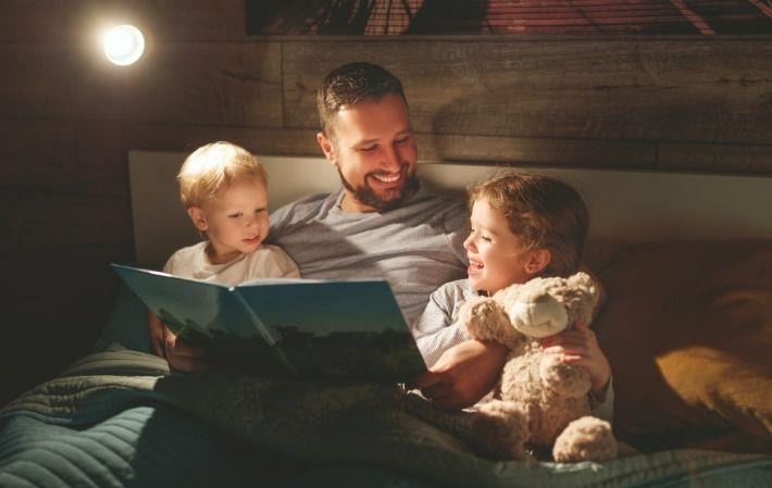 אבא מקריא לילדיו סיפור לפני השינה במיטה במטרה לבסס הרגלי שינה 