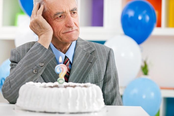 אדם מבוגר חולה אלצהיימר יושב מול עוגה ועליה נר עם סימן שאלה המסמן את הפגיעה בזיכרון 