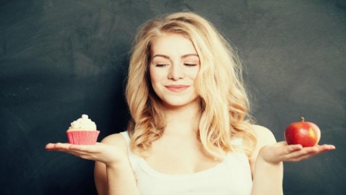 אישה מתלבטת בין אכילת עוגה לפרי כדי למנוע השמנה