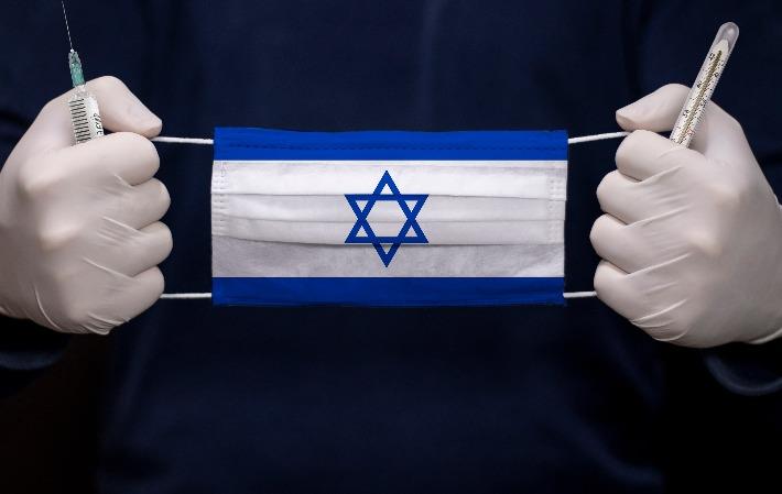 רופא מחזיק מסכה כירורגית ועליה דגל ישראל, מסמל את מאבק הצוותים הרפואיים בהתפרצות מגפת הקורונה