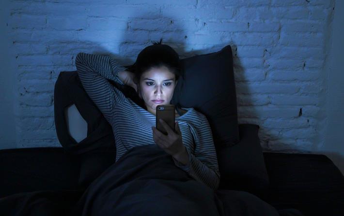 אישה מתעסקת בסמארטפון לפני השינה דבר שמוביל לדחיינות שינה 