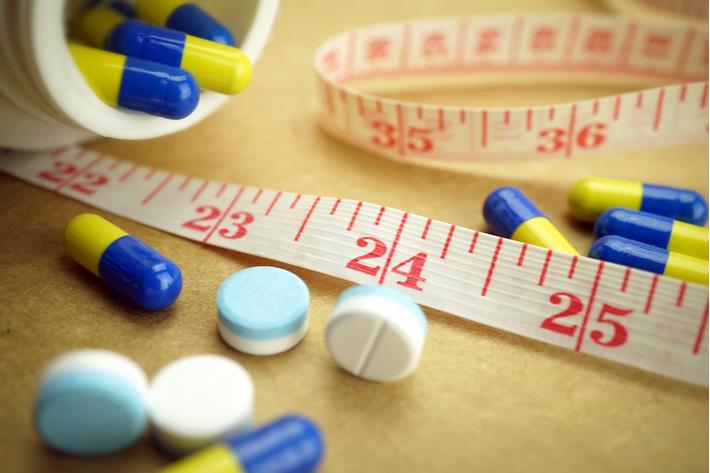 סרט מדידה ולצידו תרופות המשמשות לטיפול בהשמנה 