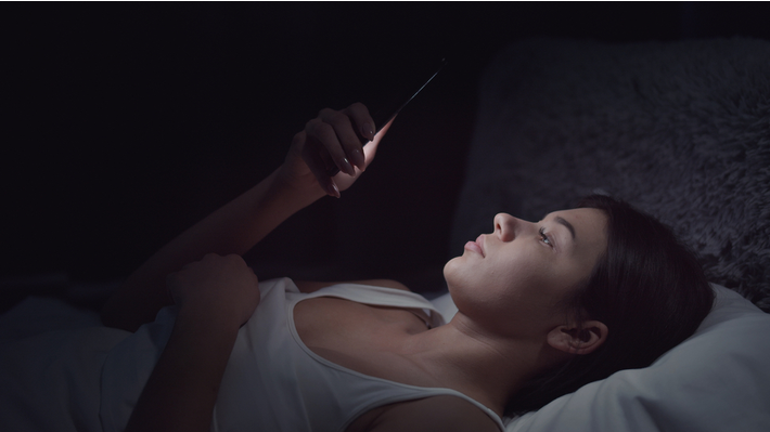 אישה צעירה עם הסמארטפון לפני השינה
