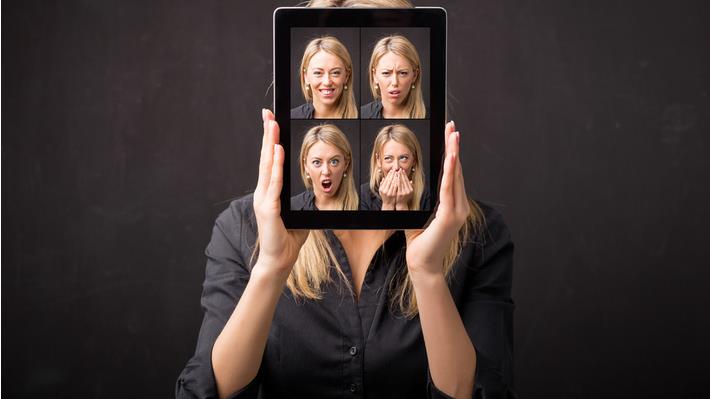 אישה מחזיקה טבלט ועליו תמונות שלה עם הבעות פנים שונות. מסמל תכונות אופי 