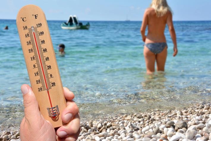 אישה נכנסת לים, יד אוחזת במד טמפרטורה. עמוס חום השפעות בריאותיות
