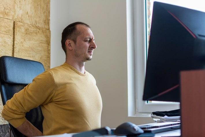 גבר יושב מול מחשב וסובל מכאבי גב תחתון