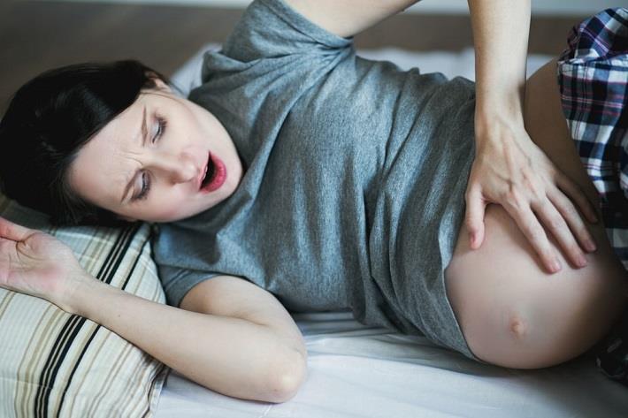 אישה עם הריון מדומה שוכבת על המיטה ונוגעת בבטן ההריונית שלה בפליאה