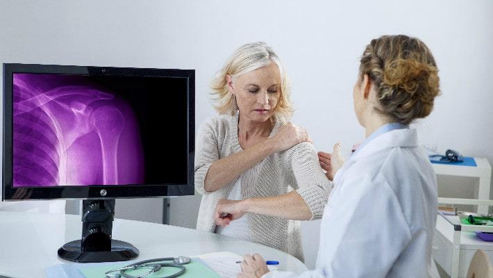 רופאה מסבירה לאישה על דלדול העצם בכתף, דנוסומאב (פרוליה) לטיפול באוסטאופורוזיס