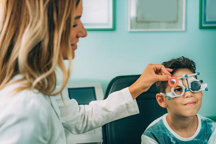רופאת עיניים מניחה מכשיר להסתרת עין אחת לצורך בדיקת עיניים לילד