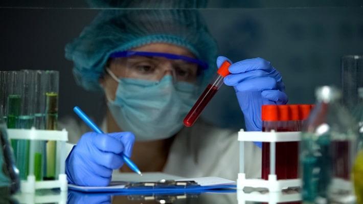טכנאית מעבדה אוחזת במבחנת דם ורושמת פרטים, בדיקת סוגי המוגלובין בדם 