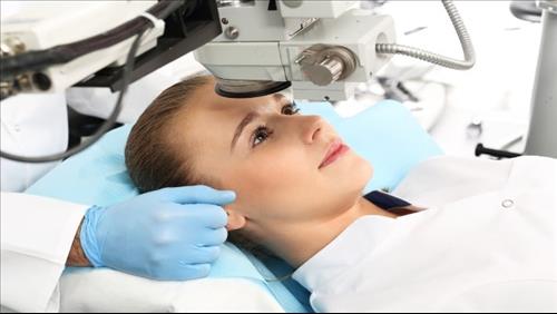 אישה שוכבת במיטת ניתוחים ומעליה מכשיר המבצע ניתוח הסרת משקפיים בלייזר
