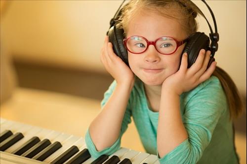 ילדה עם תסמונת דאון שמה אוזניות ליד אורגנית, טיפול במוזיקה